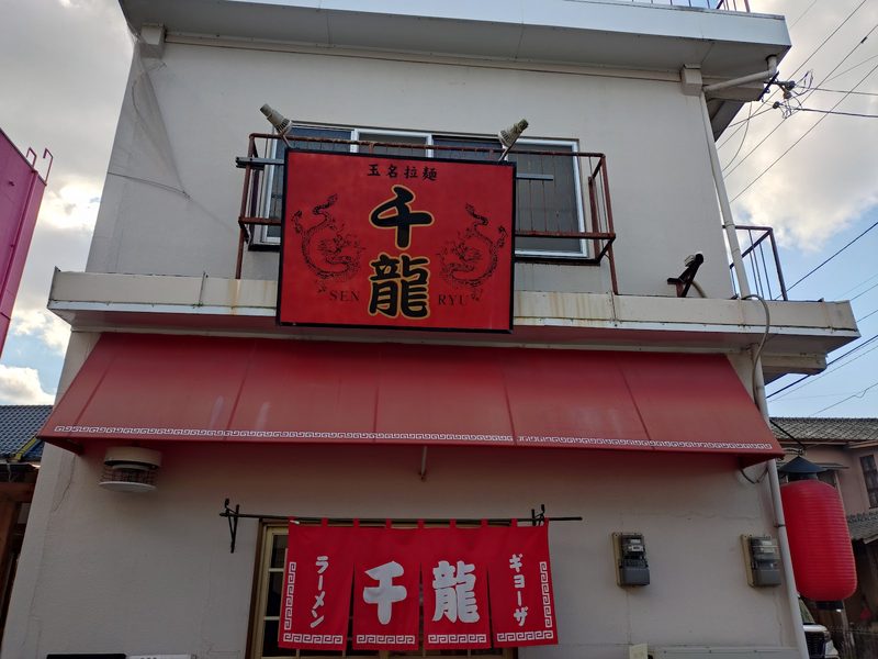 二頭の龍を描いた赤い「玉名拉麺 千龍」の看板と、赤いテント、「ラーメン 千龍 ギョーザ」の赤いのれん